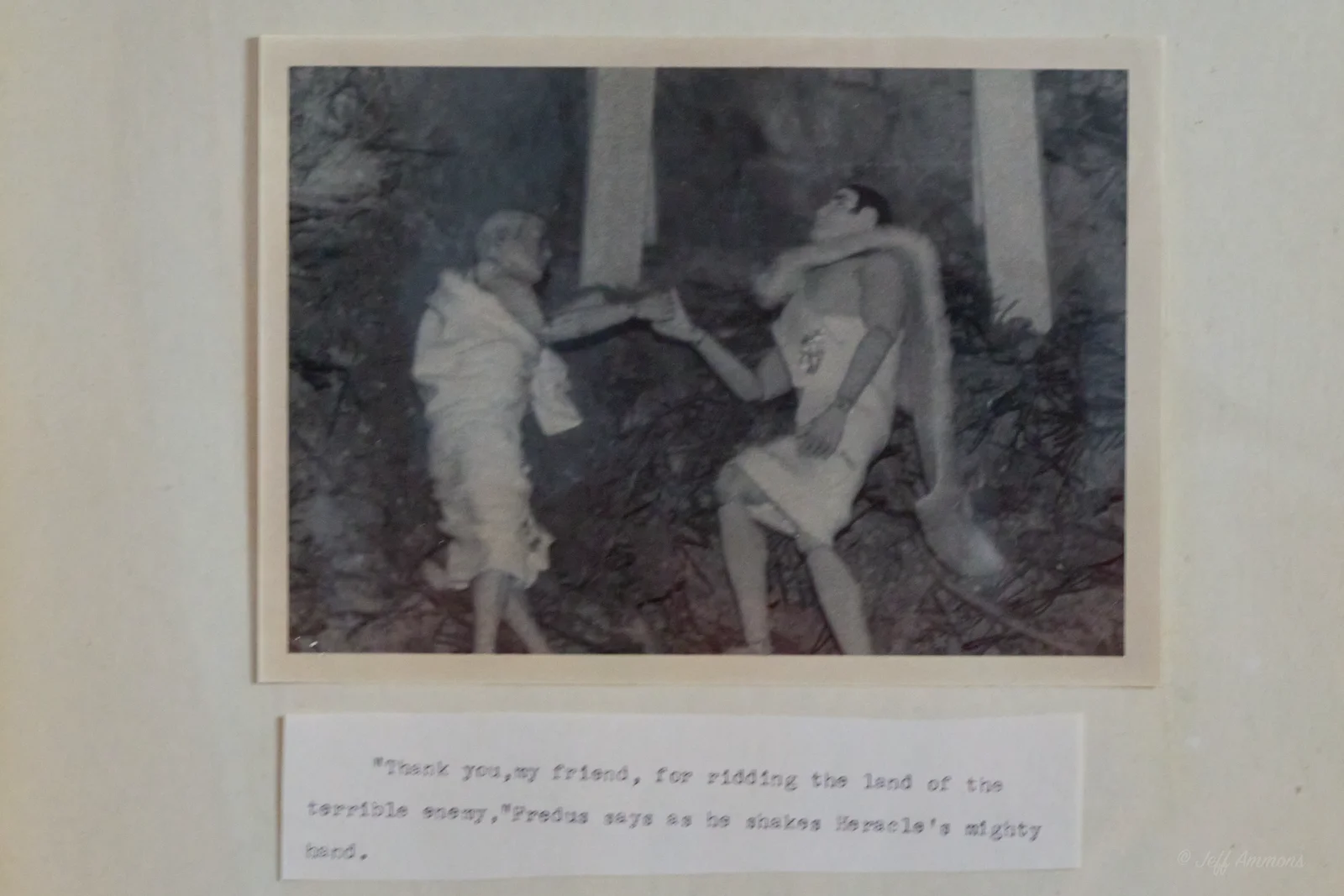 Heracles, wearing the lion's pelt as a cape, shakes hands with another robed figure in the woods.