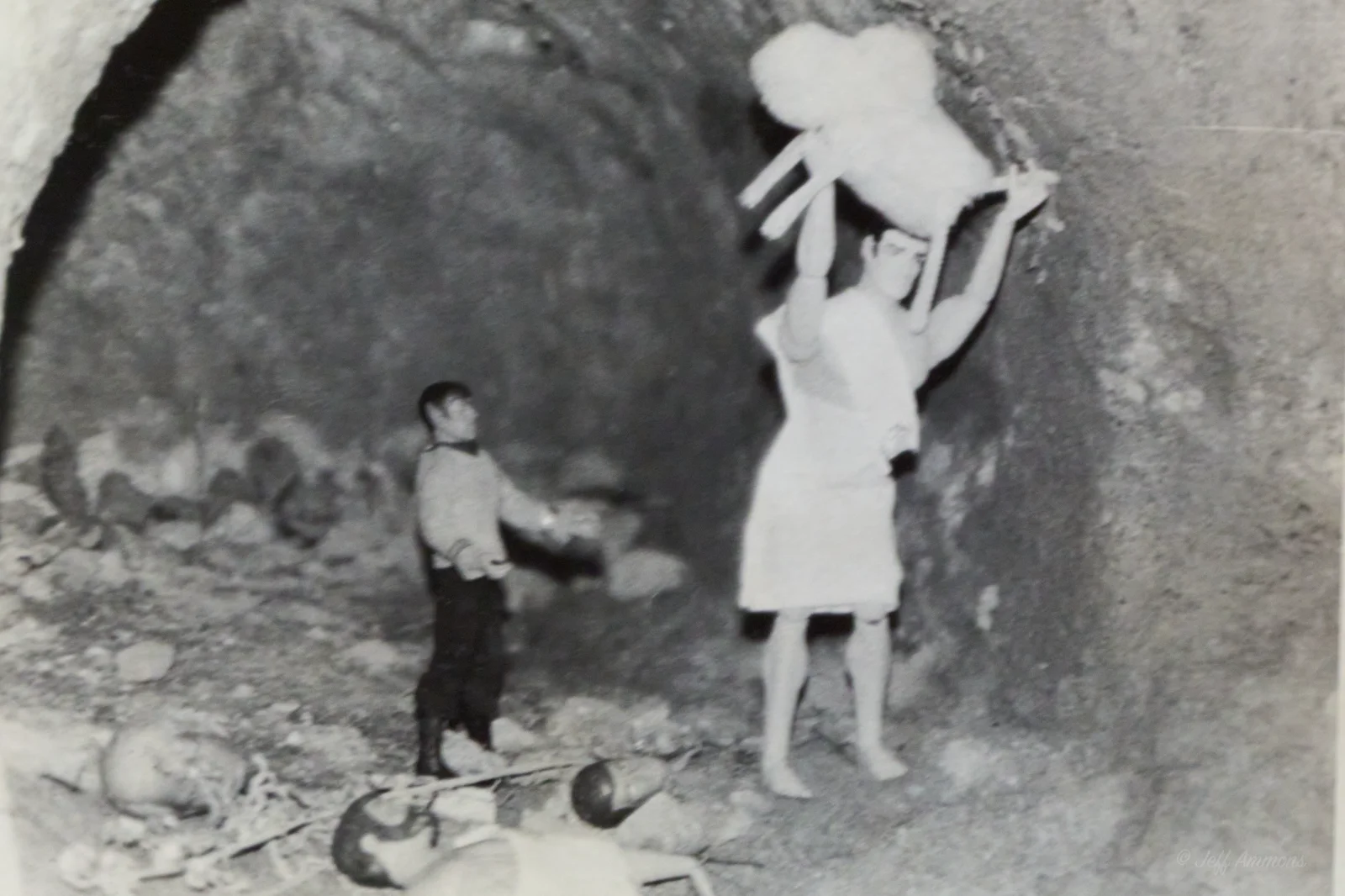 Heracles hoists the lion overhead inside the cave as Spock looks on, with bones scattered at his feet.